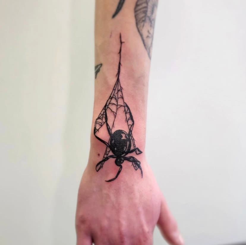 Tattoo of a spider hanging from a web on a person's forearm.