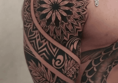 Shoulder and arm tattoo displays a mandala design, tribal patterns, and leaf elements in black ink.