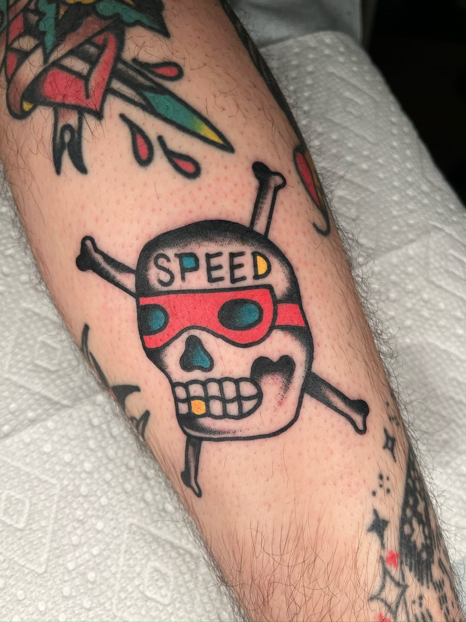 Tattoo of a skull with red goggles and the word "SPEED" on the forehead, with crossbones behind it.