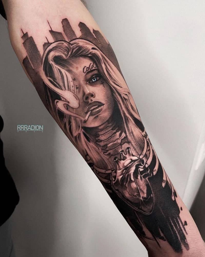 Black-and-grey forearm tattoo of a woman's face over a city skyline and an anatomical heart, carrying a small RRRADION artist watermark, with no identifiable client features in frame