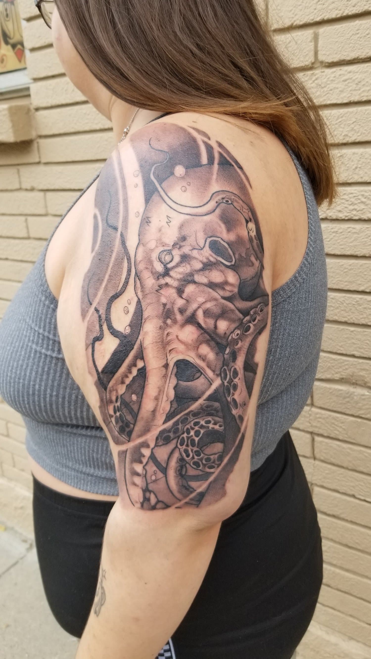 Black and grey tattoo of an octopus with the fisherman and a small lighthouse on the upper arm.