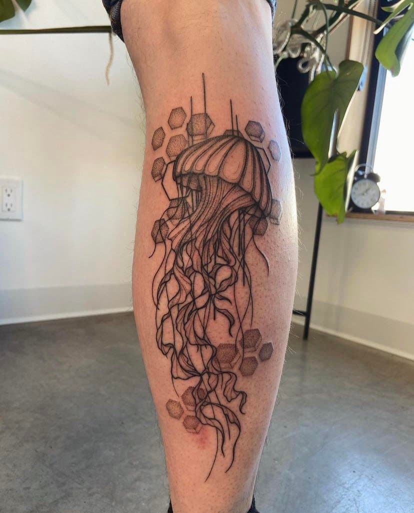 A tattoo of a jellyfish with flowing tentacles on a person's calf, surrounded by honeycomb shapes.