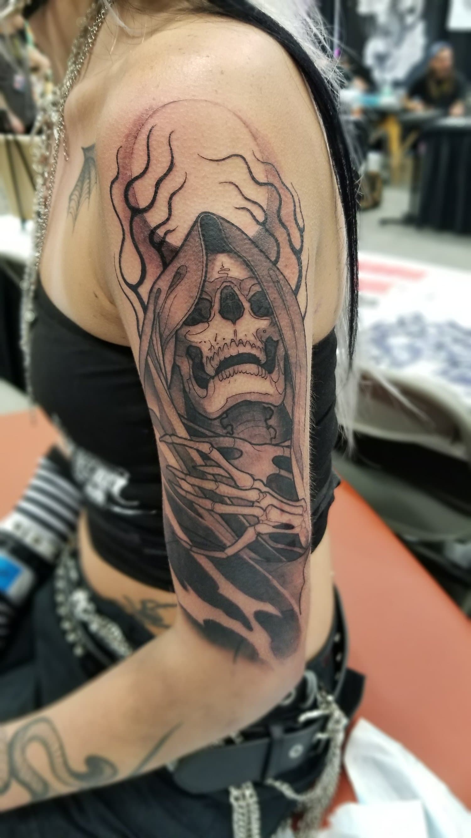 Tattoo of a skull with flowing hair on a person's upper arm, in a black and gray style.
