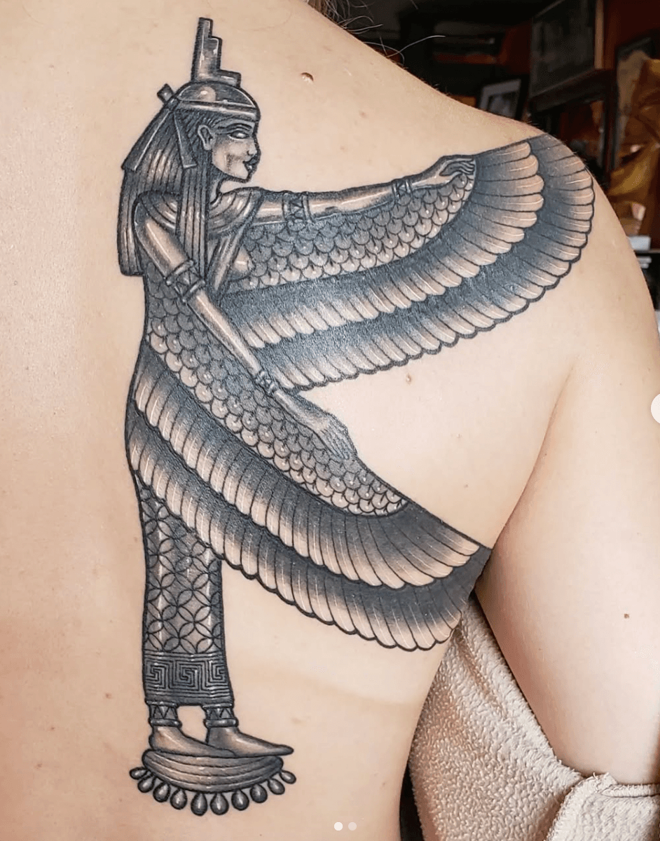 Black and gray tattoo of an ancient Egyptian figure with outstretched wings on upper arm and shoulder.