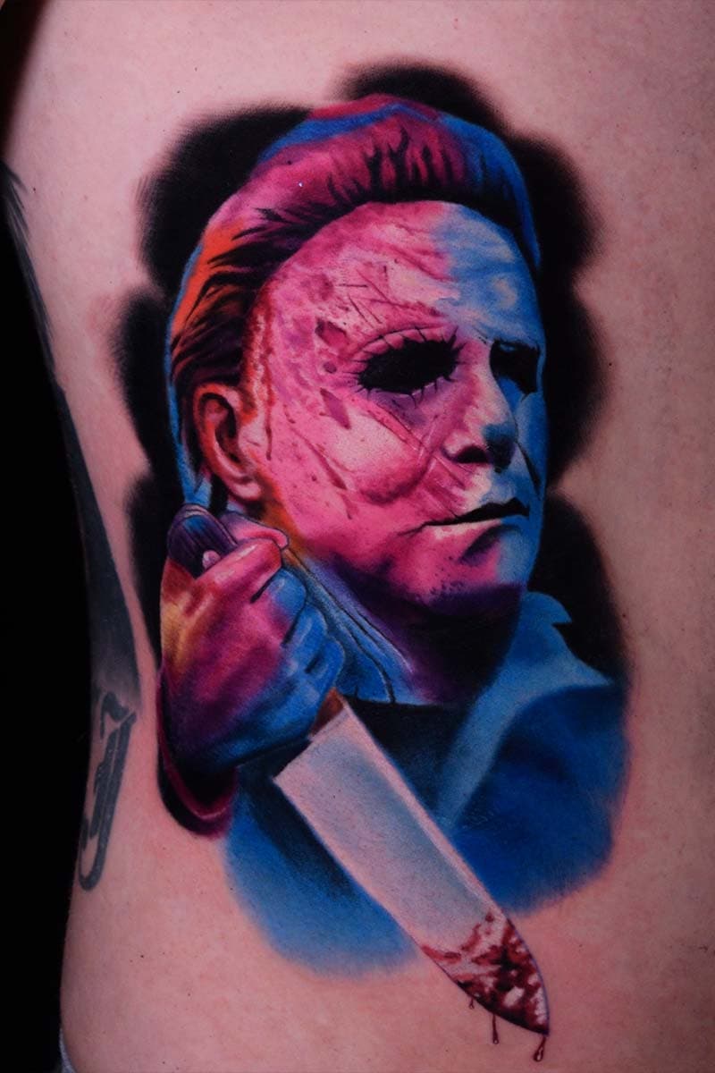 Atticus Tattoo| Colour realism tattoo of Michael Meyers holding a knife, with pink and blue inks