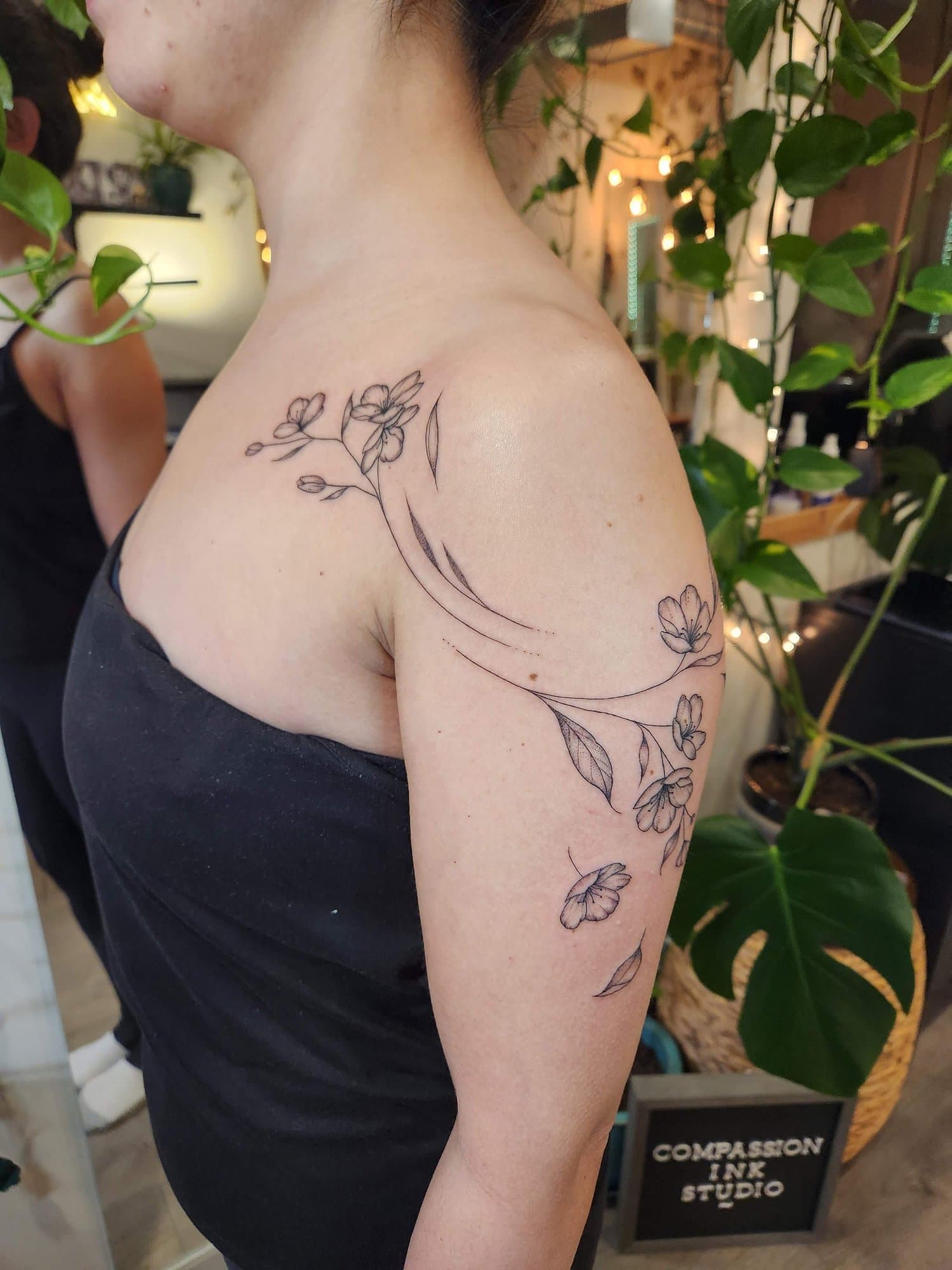 Fine-line flowering branches flowing from the chest across the shoulder and upper arm