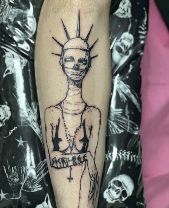 Tattoo of a bare-chest nun wearing a headpiece, rosary, mouth covering, and tape to cover their nipples. The word "Sacrilege" written across their arm.