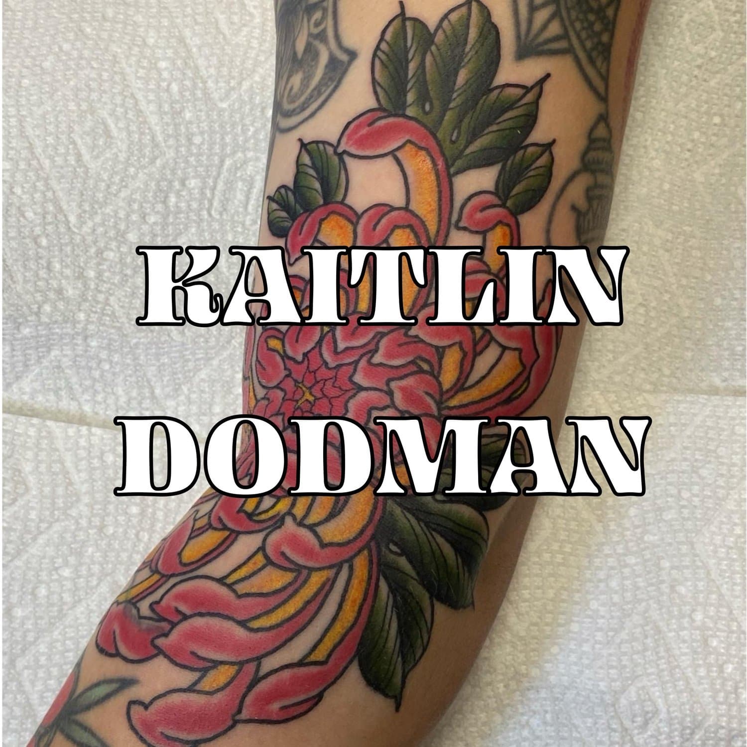 Tattoo By Kaitlin Dodman of a Pink and Yellow Chrysanthemum with green leaves on a persons arm.