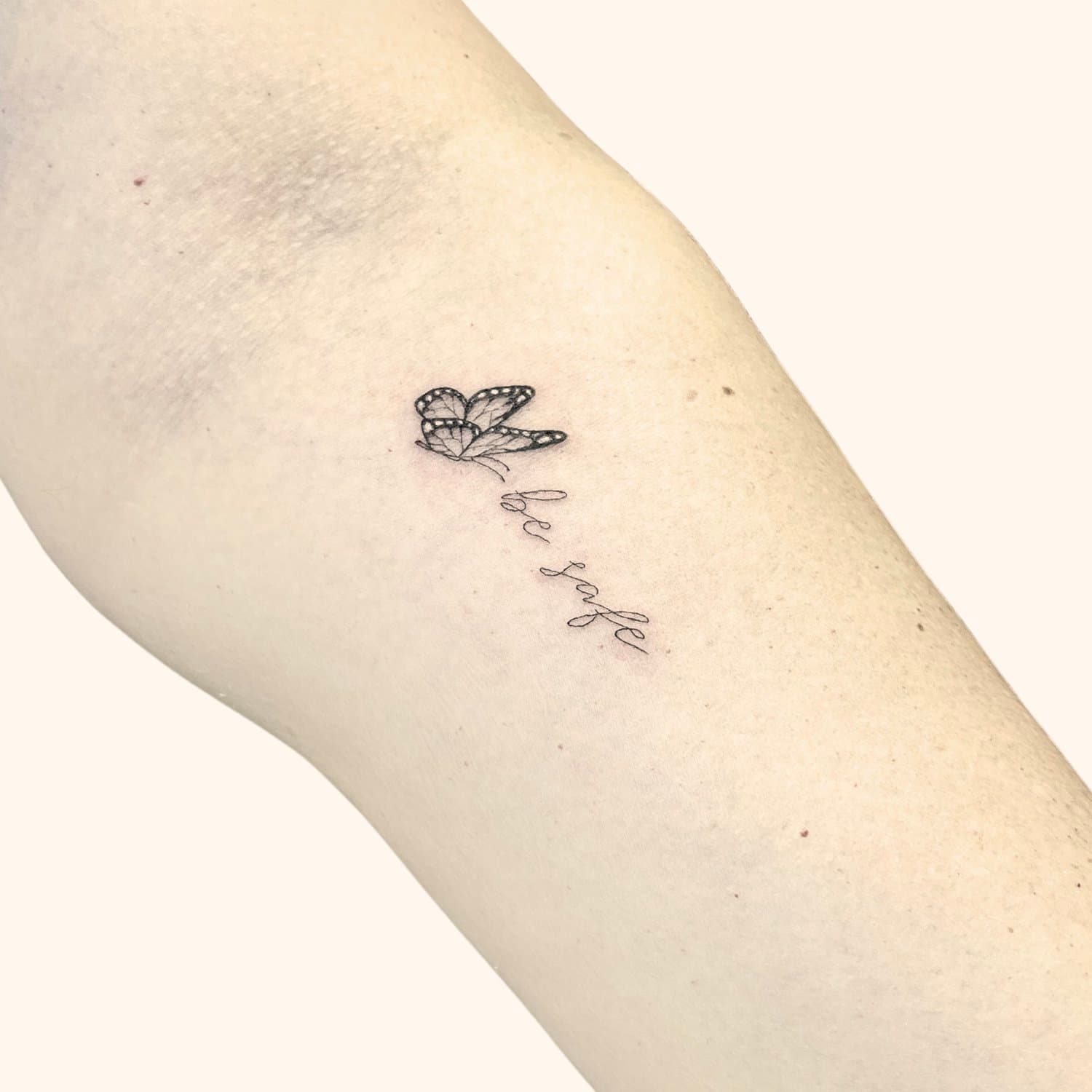 Tattoo of a butterfly above the phrase 'be safe' on a person's arm.