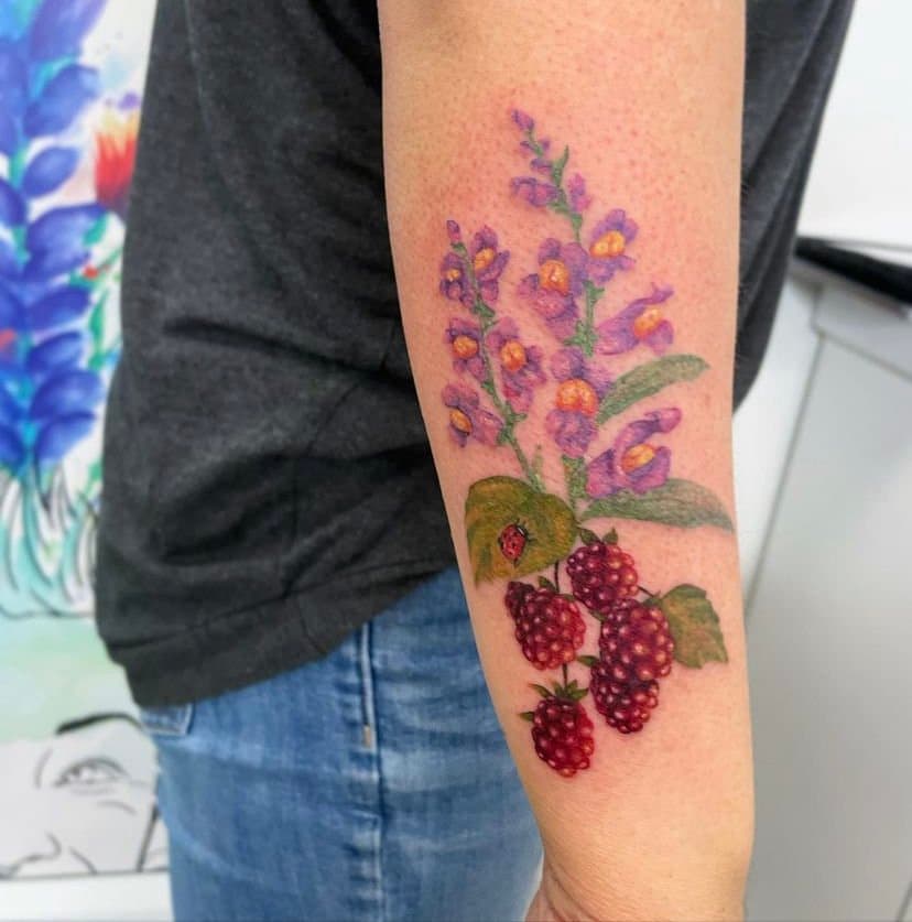 Colorful tattoo of purple flowers, green leaves, a ladybug, and red berries on person's forearm.