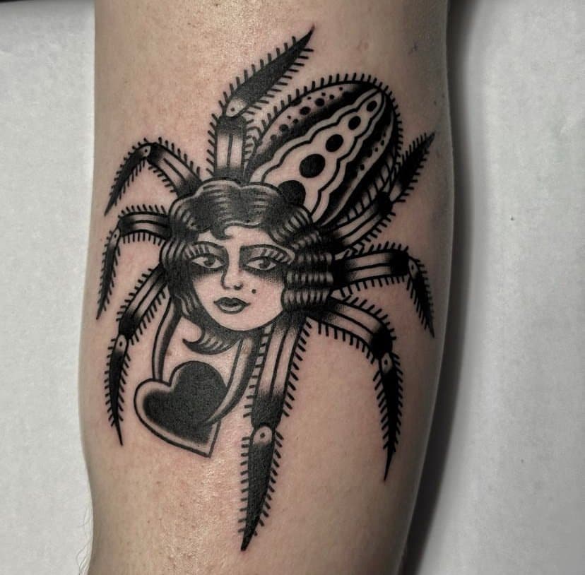 Tattoo of a spider with the body replaced by a woman's face and a heart hanging from her neck.
