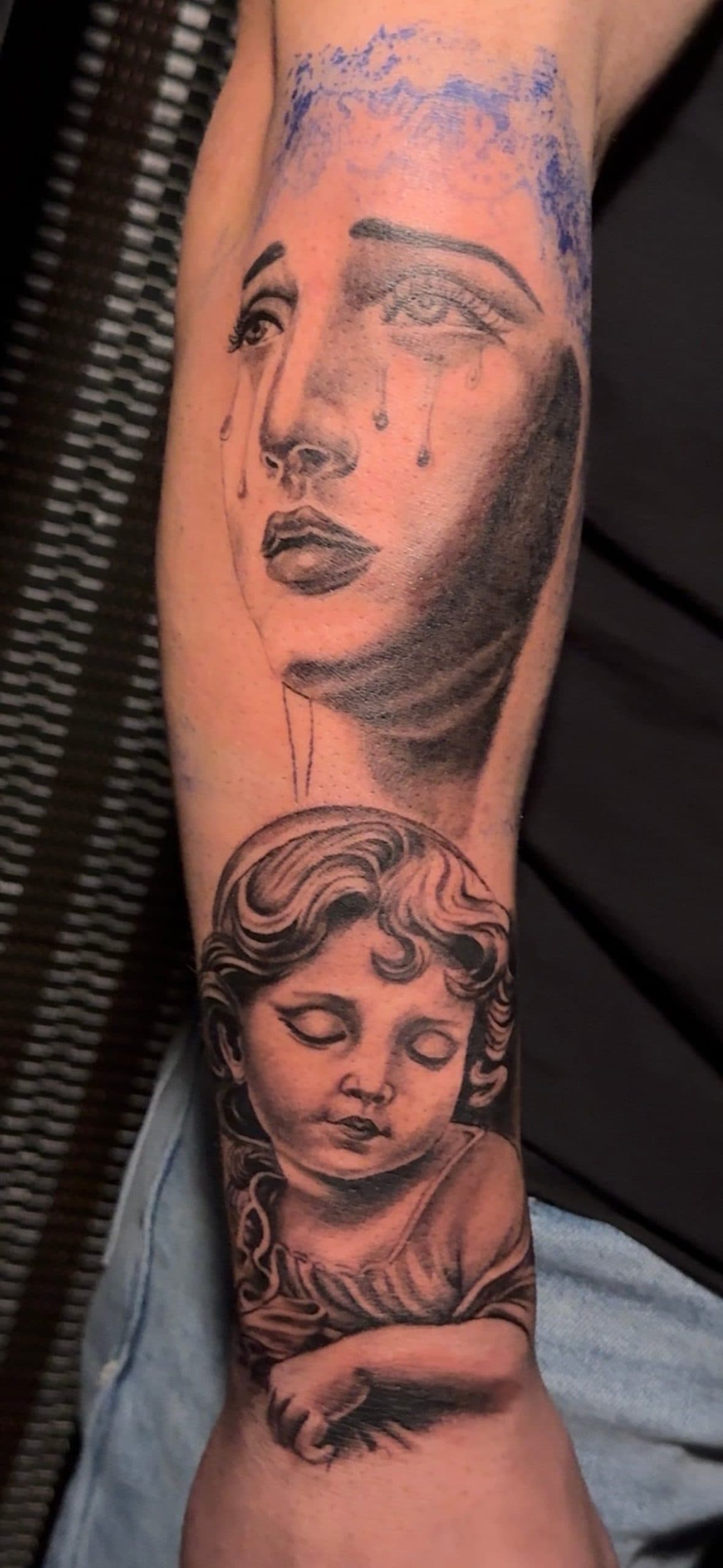 Weeping woman and child tattoo in black and grey ink on a forearm.
