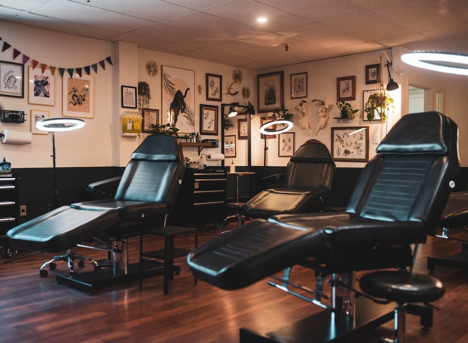 Interior of a Black Eleven Tattoo studio in Halifax featuring three black reclining tattoo beds, framed artwork, plants, and ring lights used by the tattoo arti