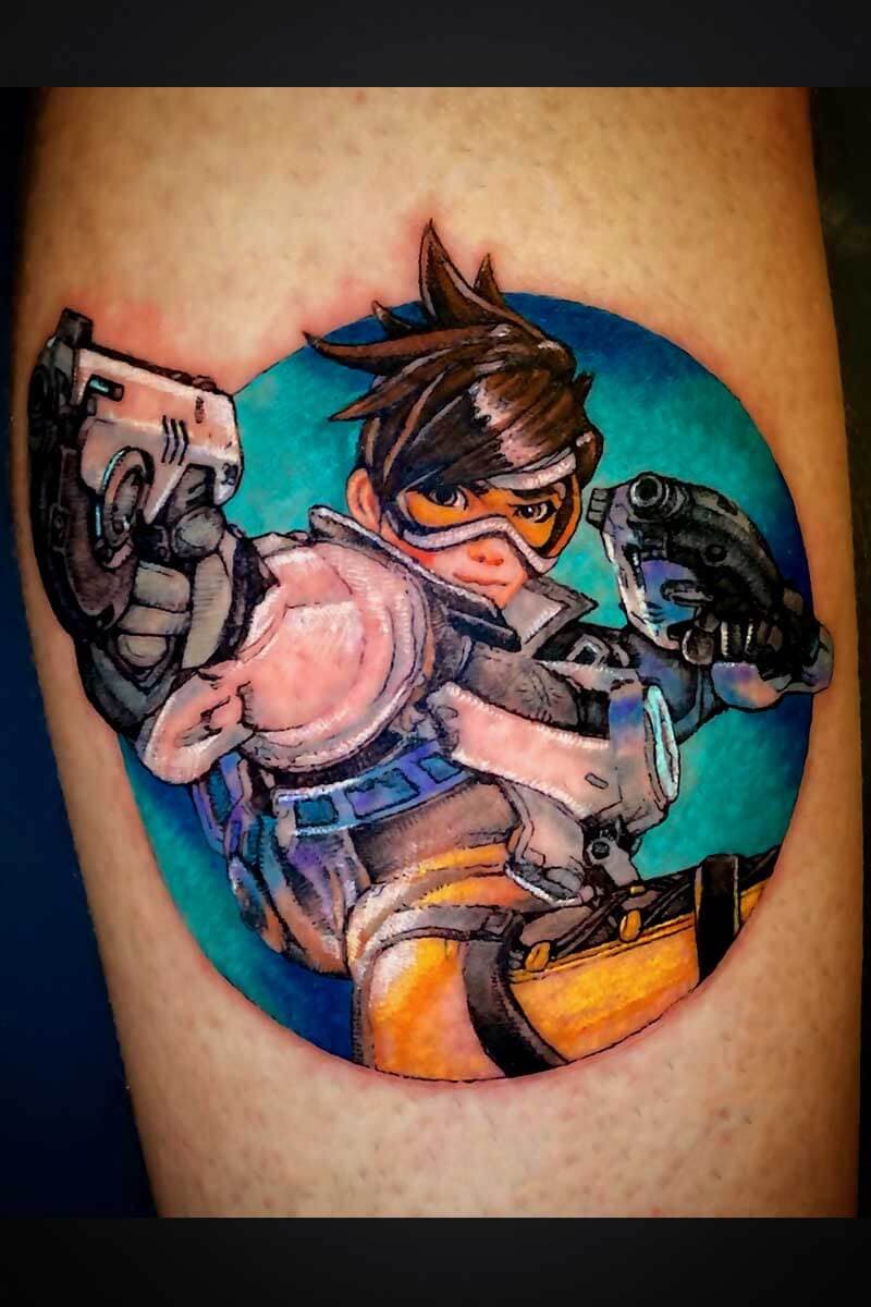 Colorful tattoo of a female video game character in orange and brown combat gear with goggles, posed mid-action against a teal circle background.