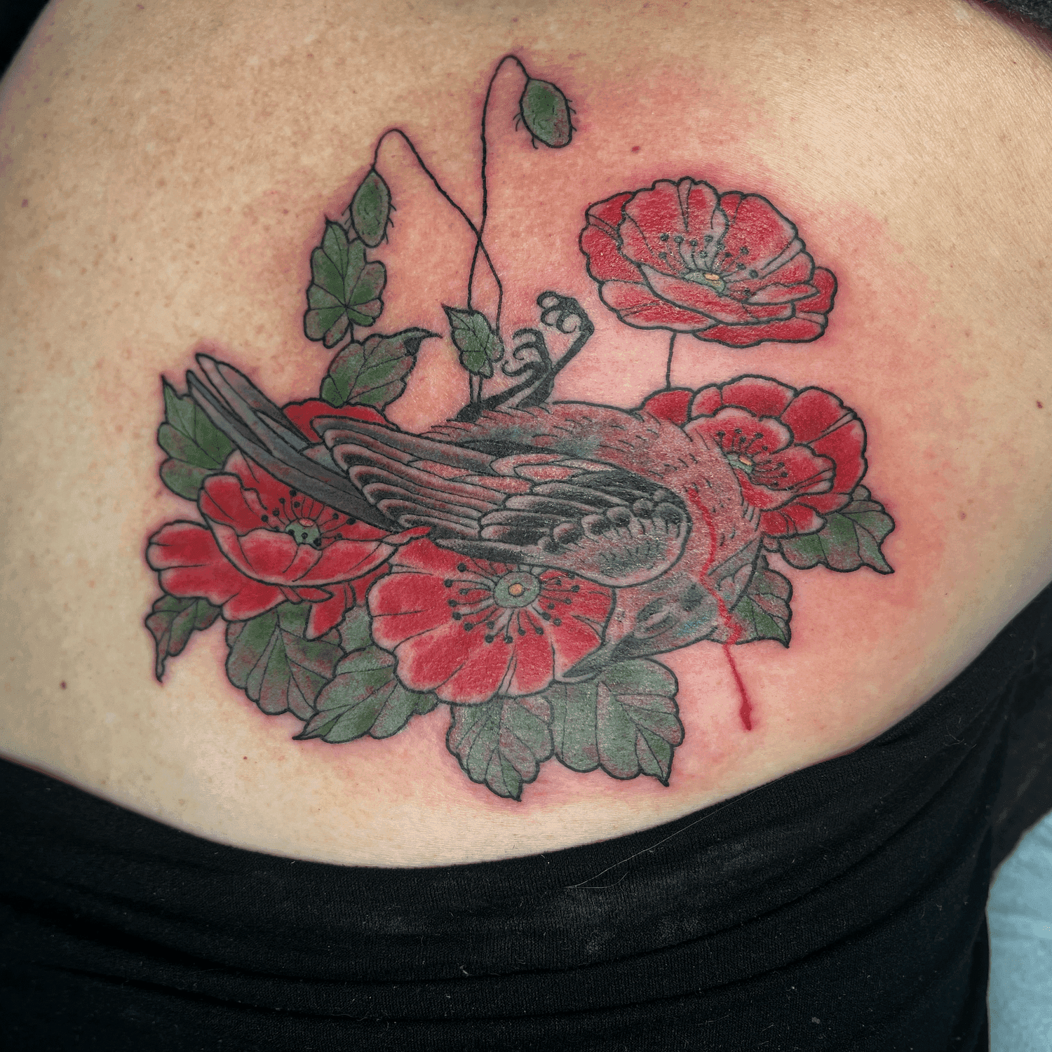 Tattoo of a bird with red flowers and green leaves on skin