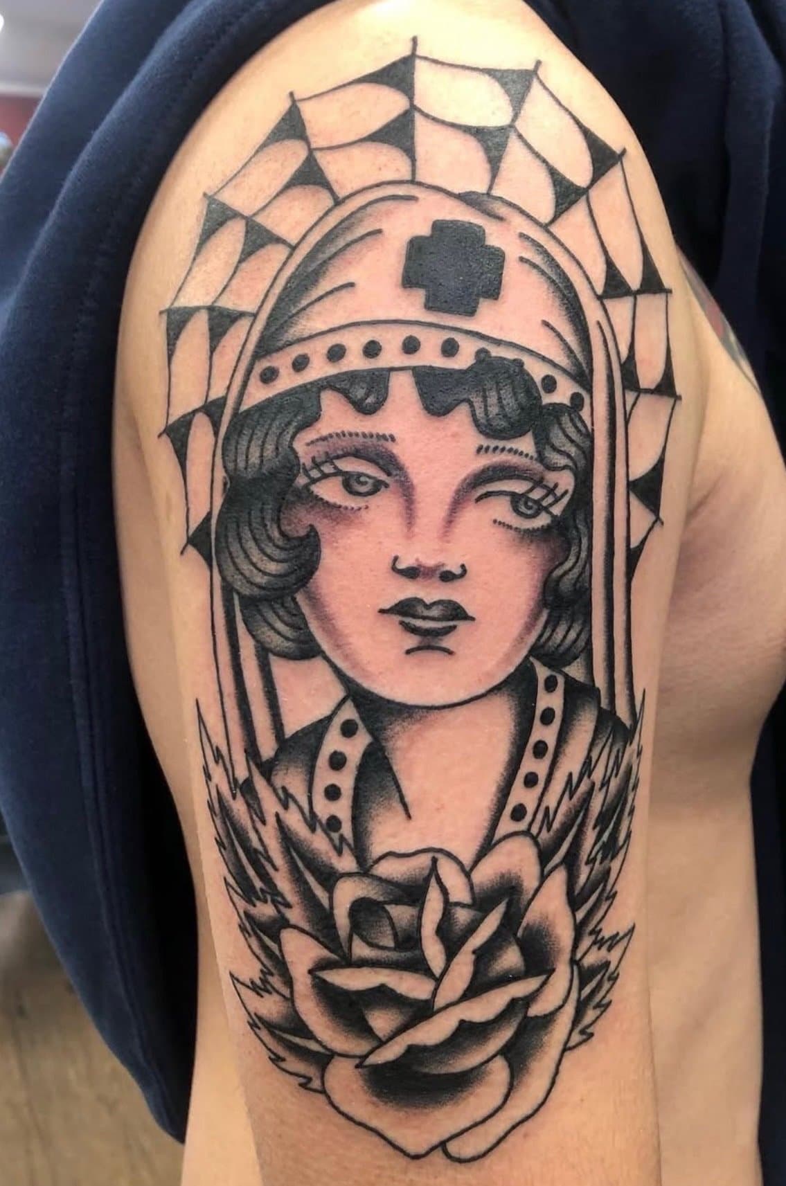Tattoo of a nurse with a head covering, surrounded by a spider web and a blooming rose at the bottom.
