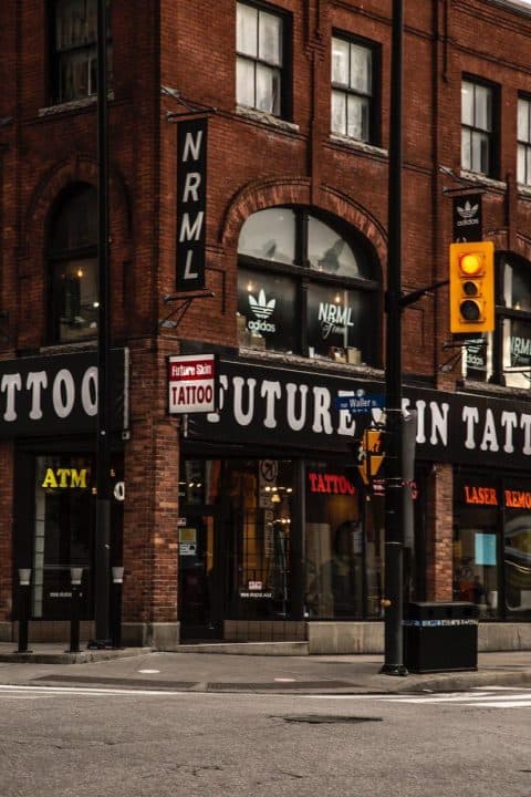 Brick building with 'FUTURE SKIN TATTOO' and 'NRML' signage, an Adidas logo, ATM, street view, and a yellow traffic light.