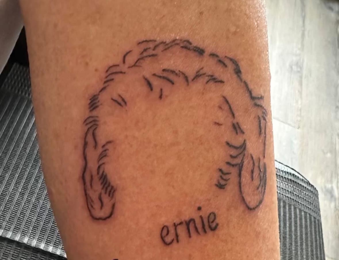 Fine line tattoo of dog ears and pet's name "Ernie" beneath