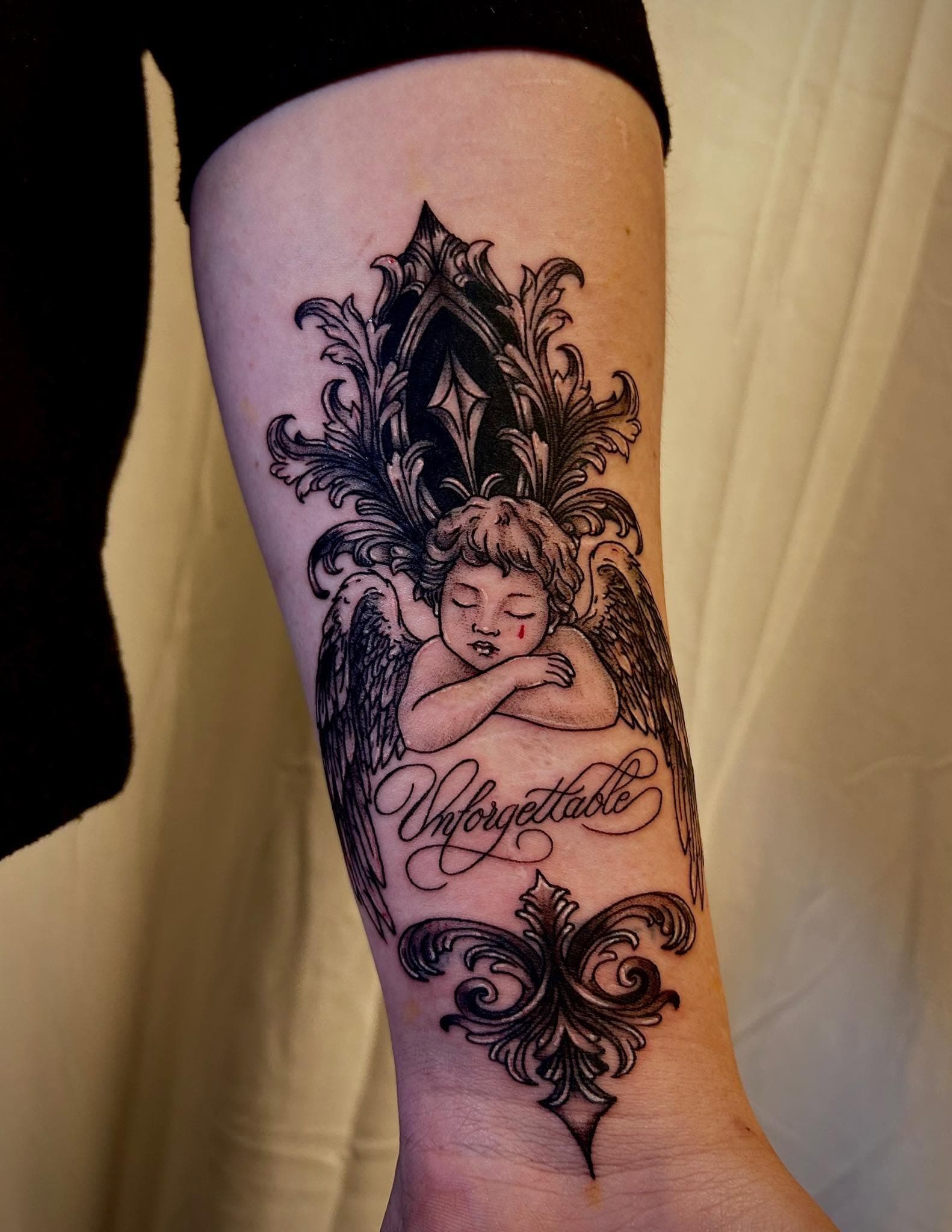 Tatouage noir et gris d'un chérubin endormi avec lettrage Unforgettable