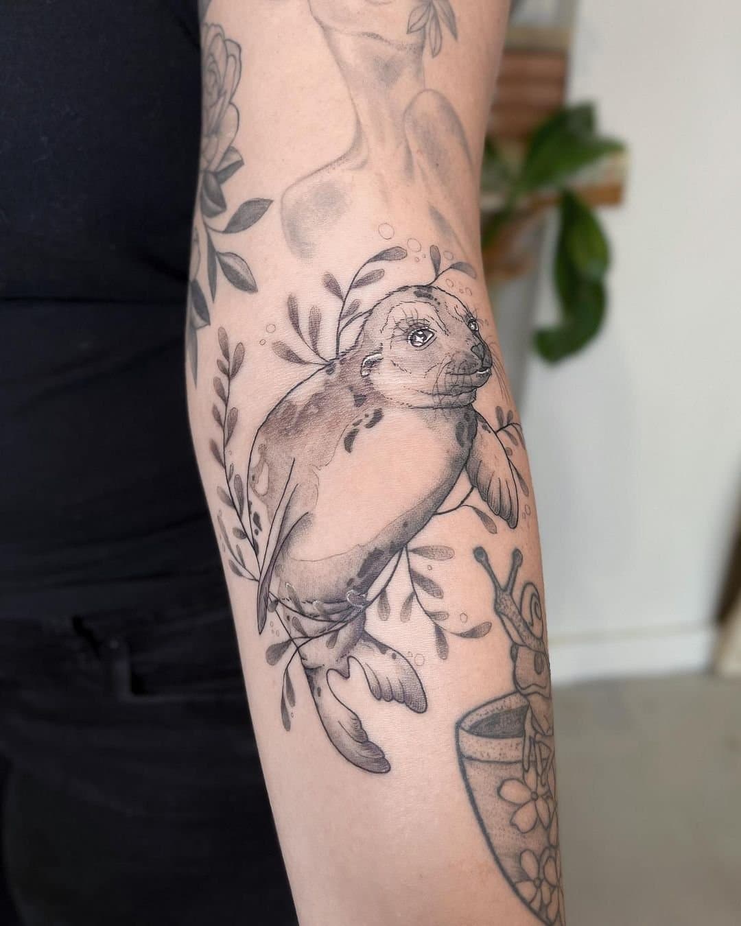 Illustrative forearm tattoo of a seal surrounded by botanical and aquatic elements