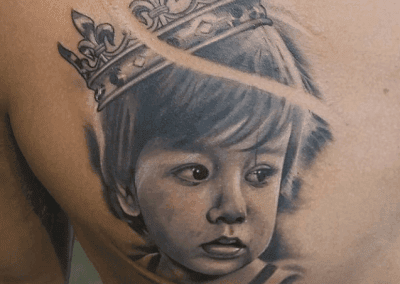 Chest tattoo of a child's portrait wearing a crown, rendered in detailed black and gray ink.