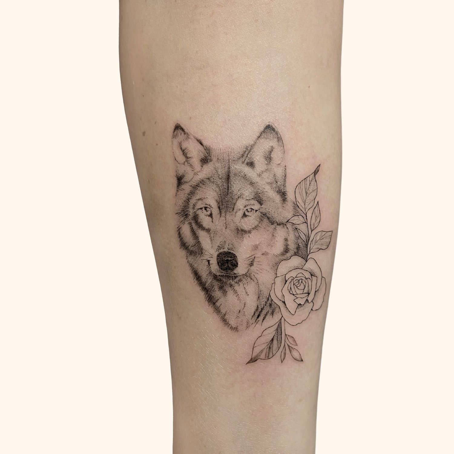 A tattoo of a wolf's face with a rose and leaves on a person's leg.