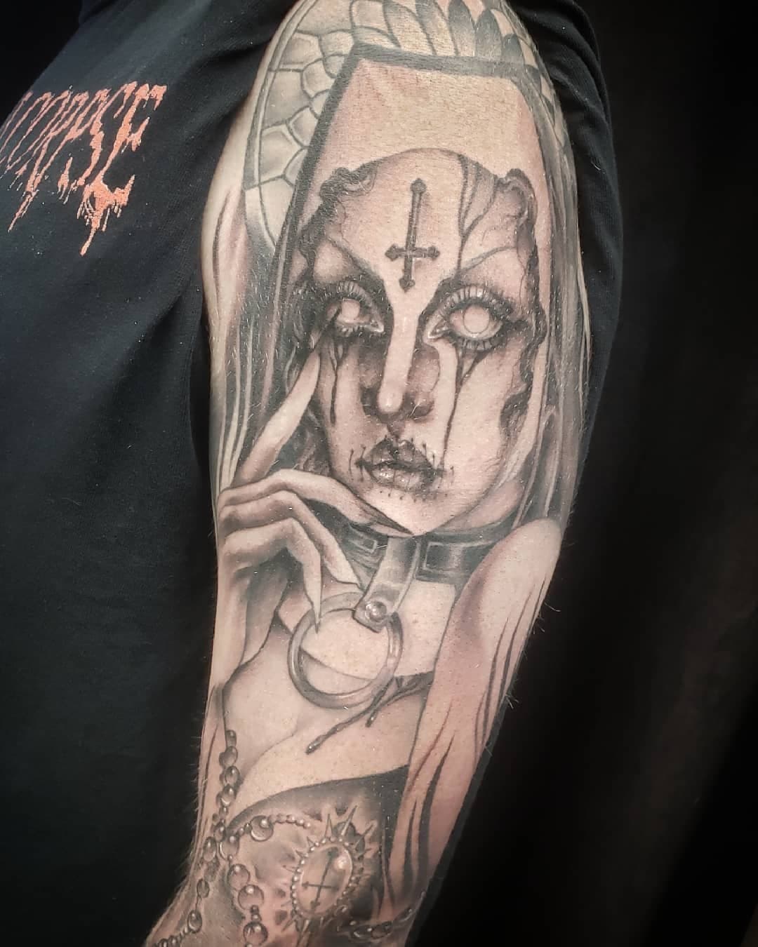 Black and gray tattoo of a woman with a solemn expression, tears streaming down her face, holding a mirror. She has a cross symbol on her forehead, and there is