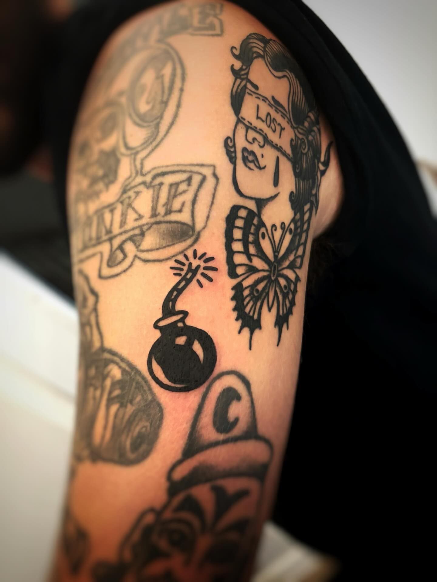 Tattooed arm with bomb, blindfolded woman, and butterfly designs