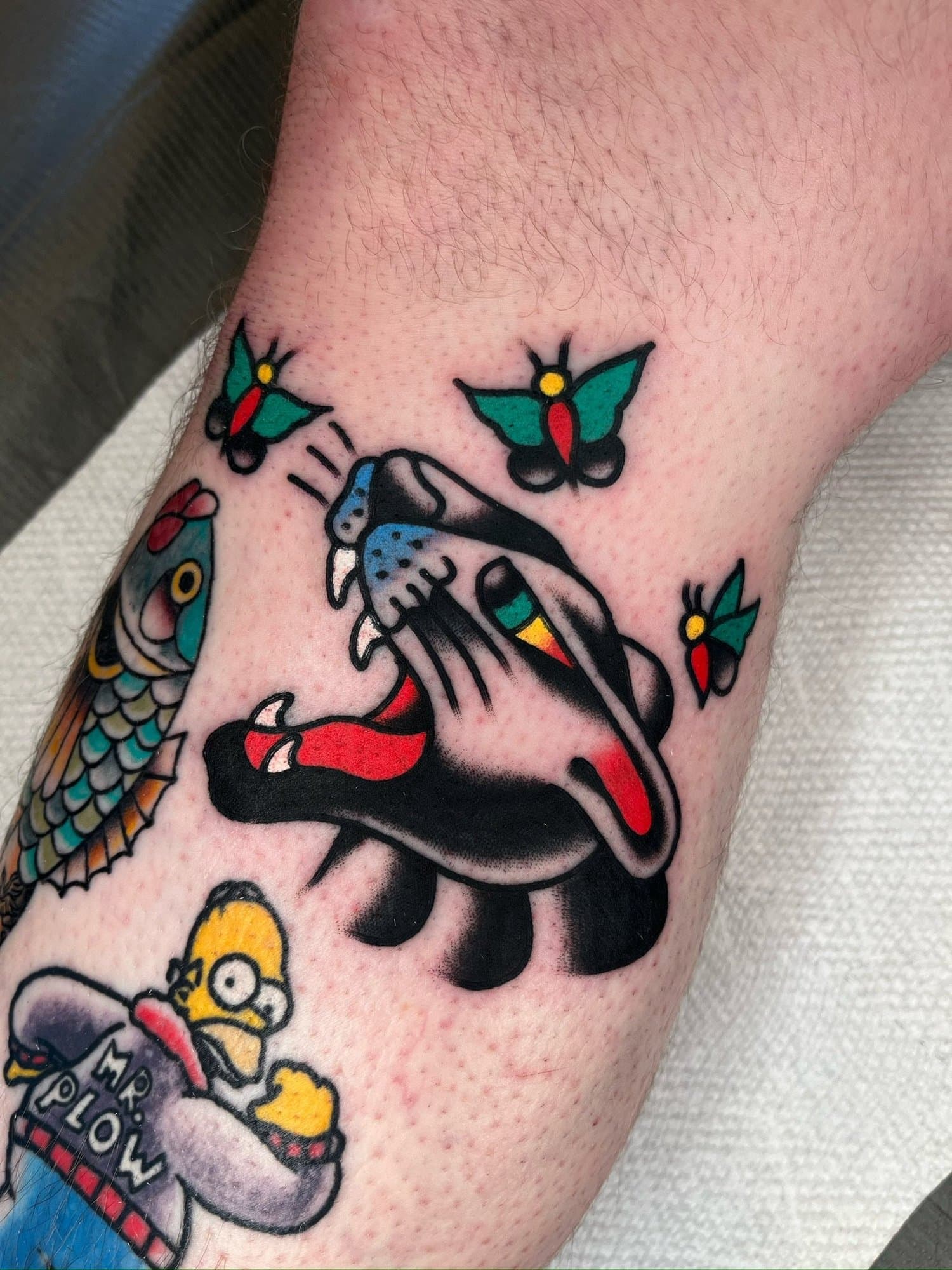 Tattoo of a traditional panther with its mouth open, surrounded by colorful butterflies on a person's arm.
