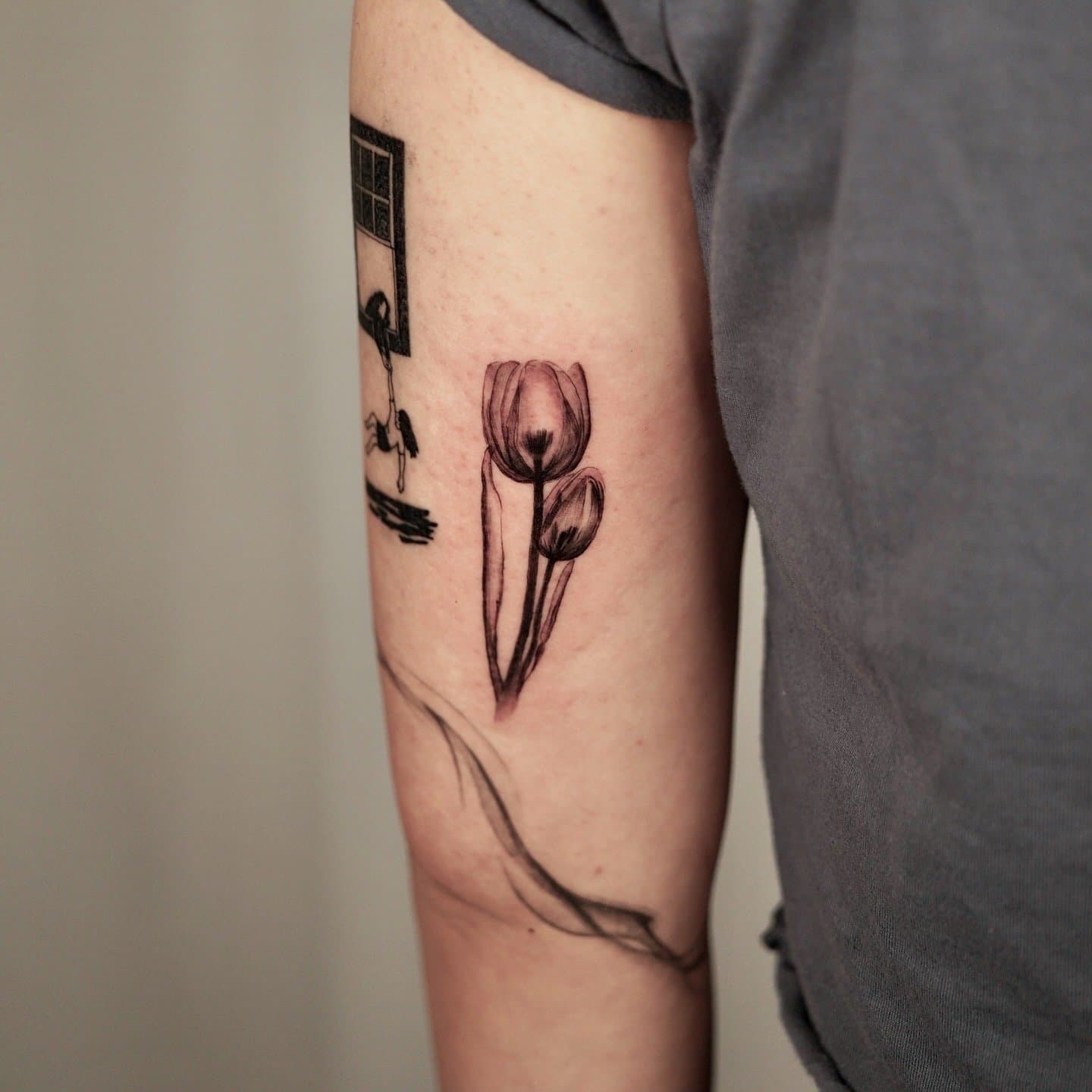 Tattoo of three tulips on a person's arm, with a black and white design of a window or door in the background.