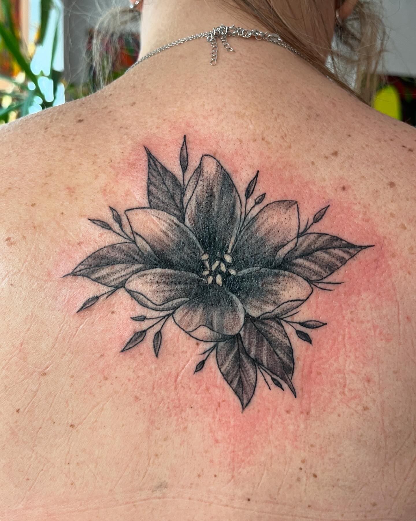 Black and grey floral tattoo on a person's upper back depicting a large flower with leaves.
