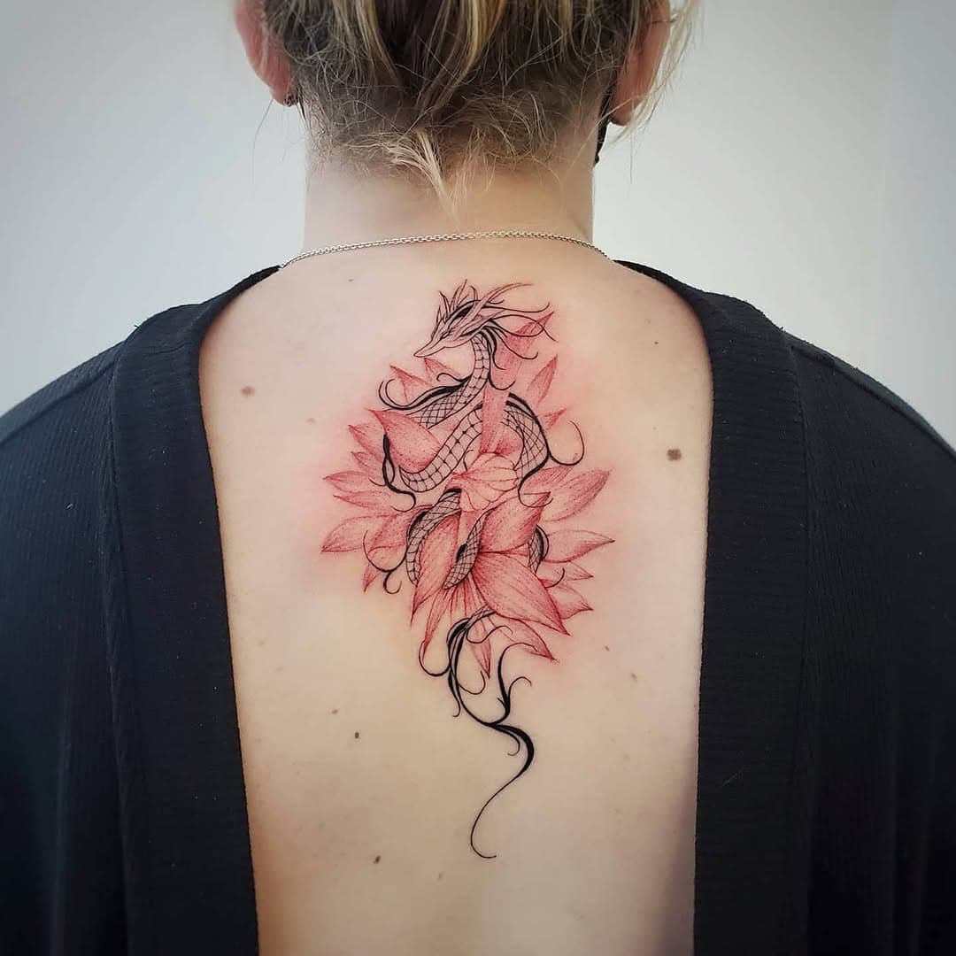 Upper-back tattoo of a black linework dragon over red lotus flowers
