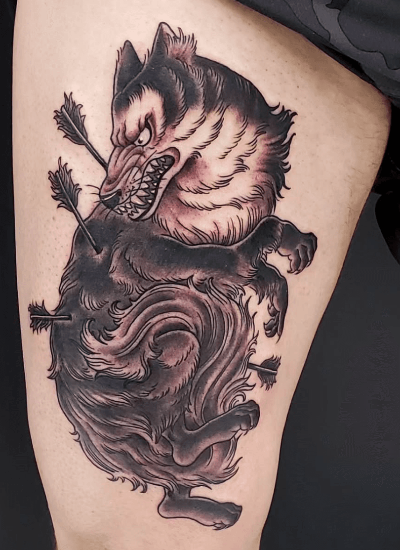 Tattoo of a fierce wolf with an arrow piercing through its body, depicted in a traditional black and gray style.