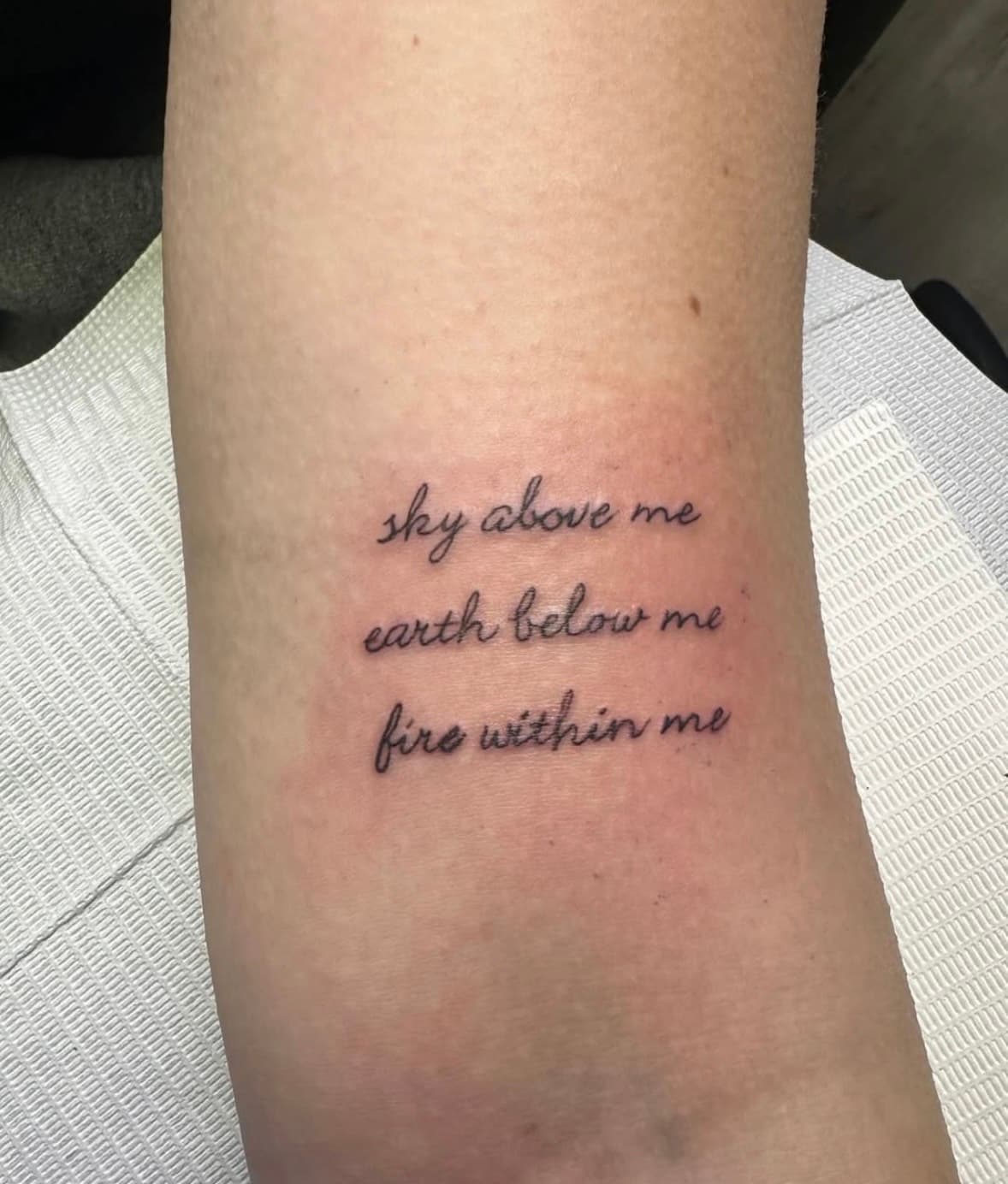 Script tattoo that reads "Sky above me, earth below me, fire within me"