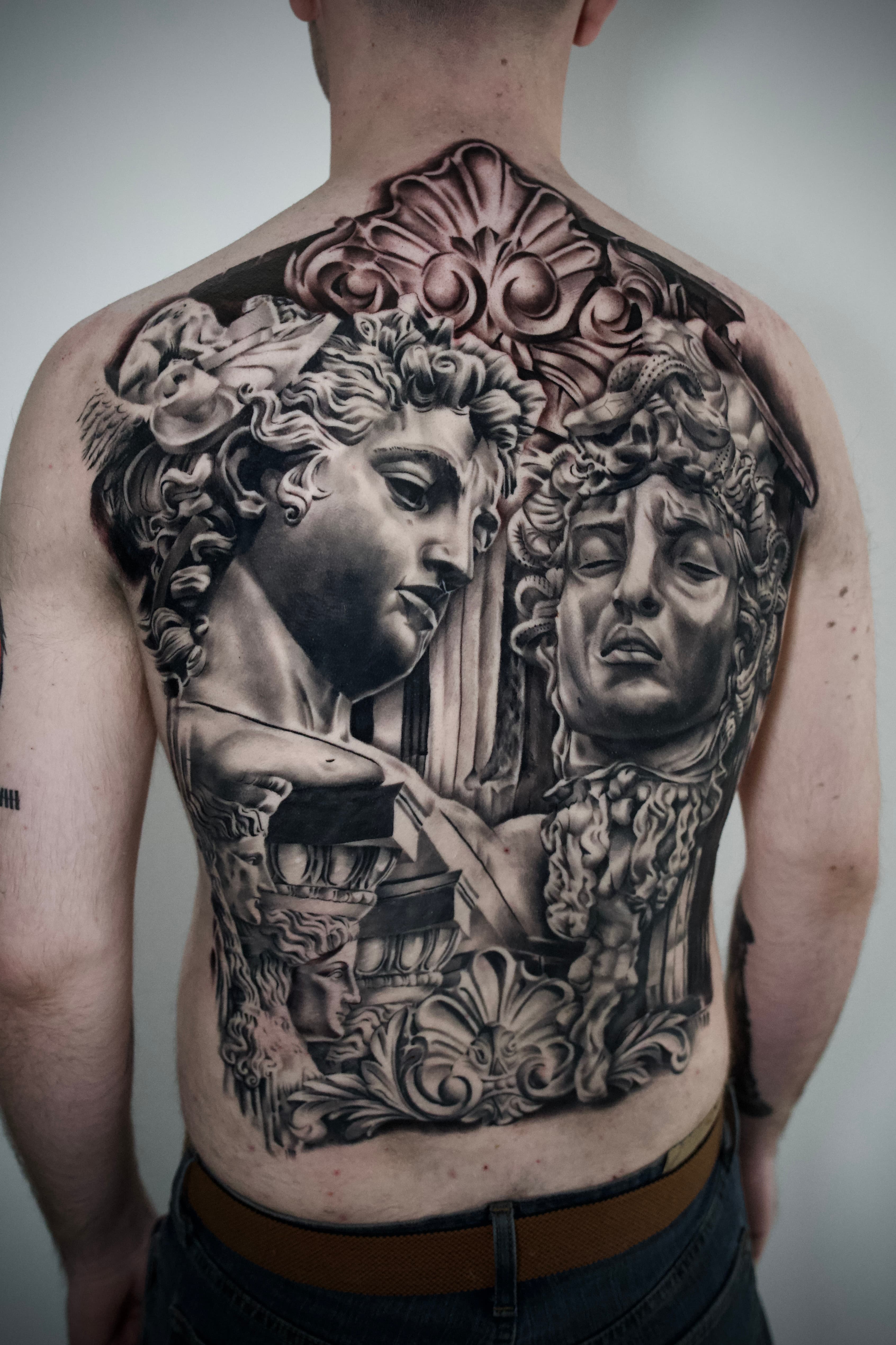 Black-and-grey full-back composition with classical busts, Medusa imagery, and ornate architectural framing