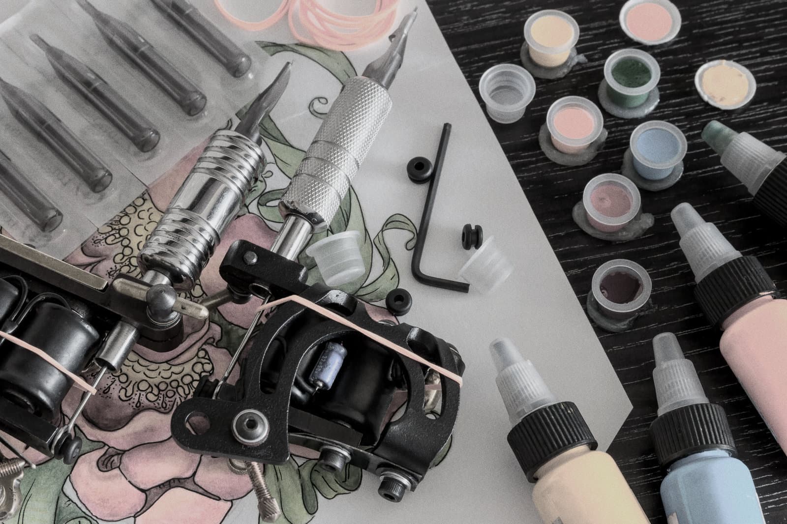 Tattoo supplies including ink caps, tattoo machine, and tools arranged as a background image.