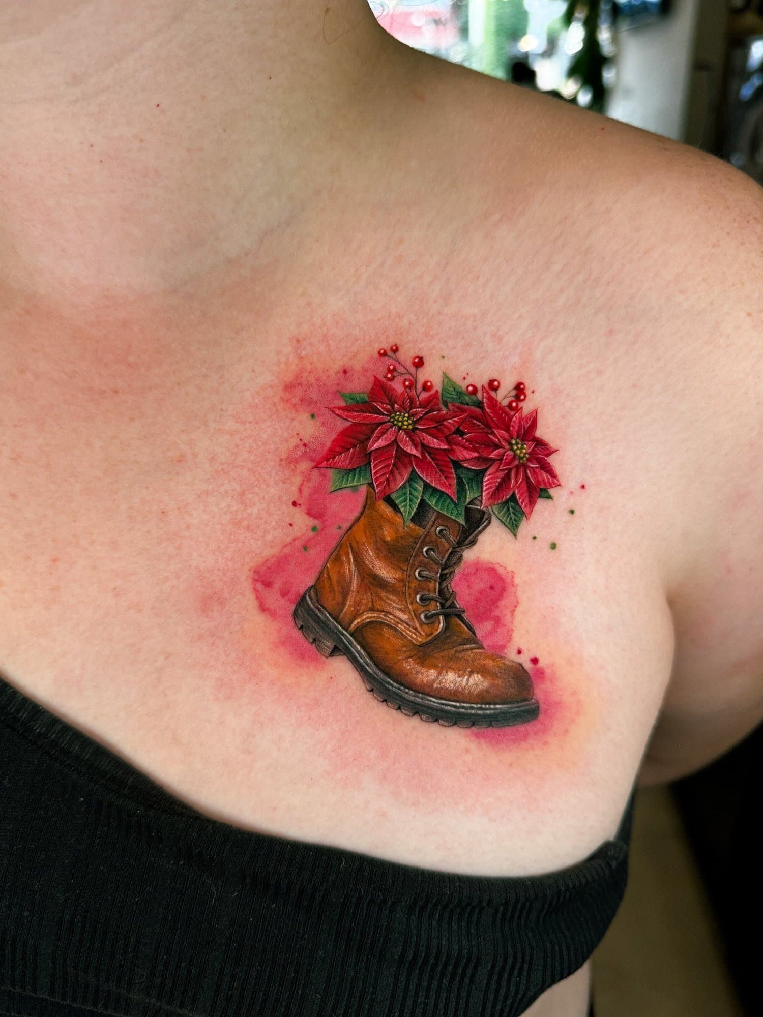 Tattoo of a brown leather boot with red poinsettia flowers and green leaves emerging from the top, on a person's chest.