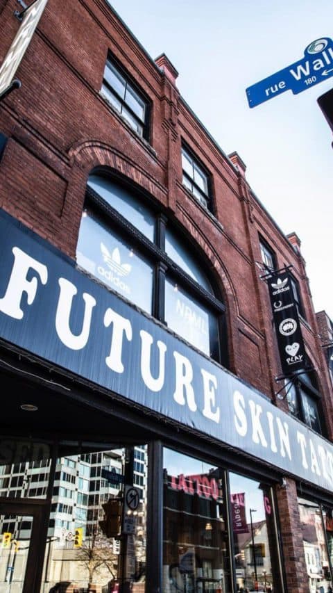 Future Skin Tattoo store in a brick building with Adidas logos in the window and on hanging banners.