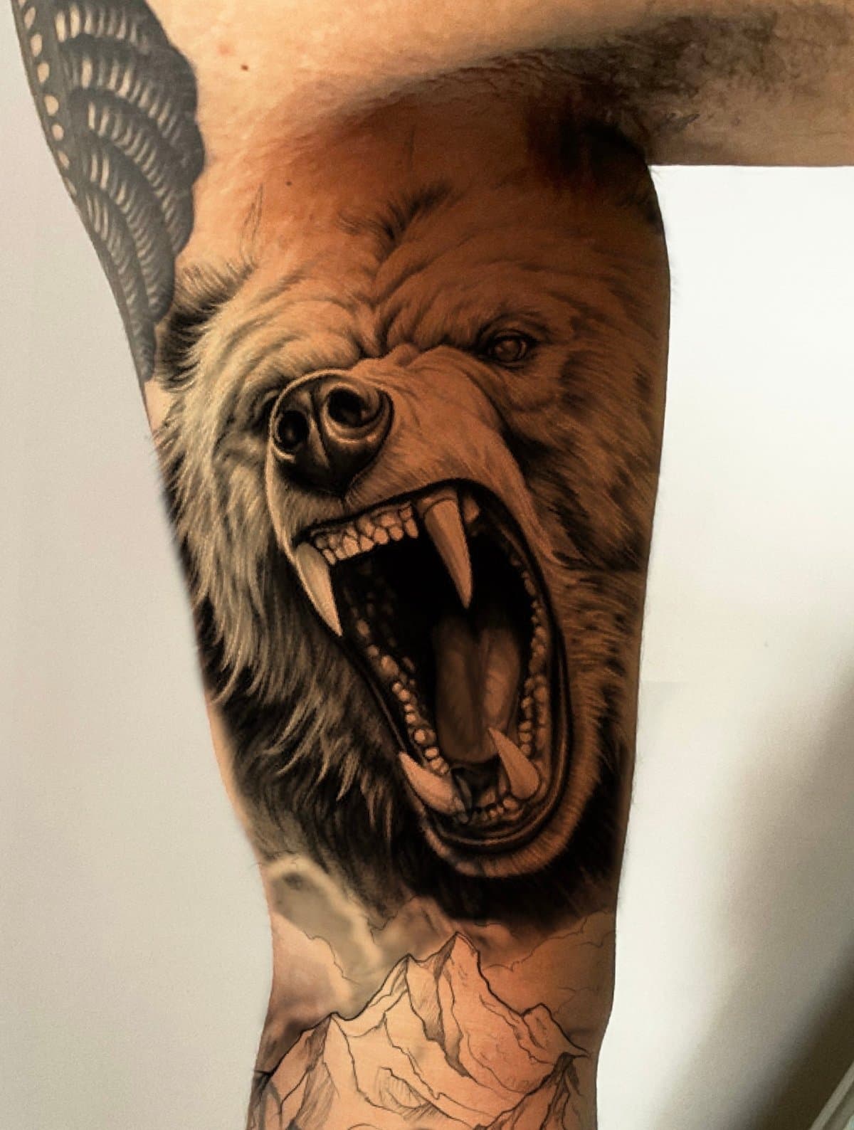 Roaring bear tattoo with visible fangs and mountain range on a thigh.