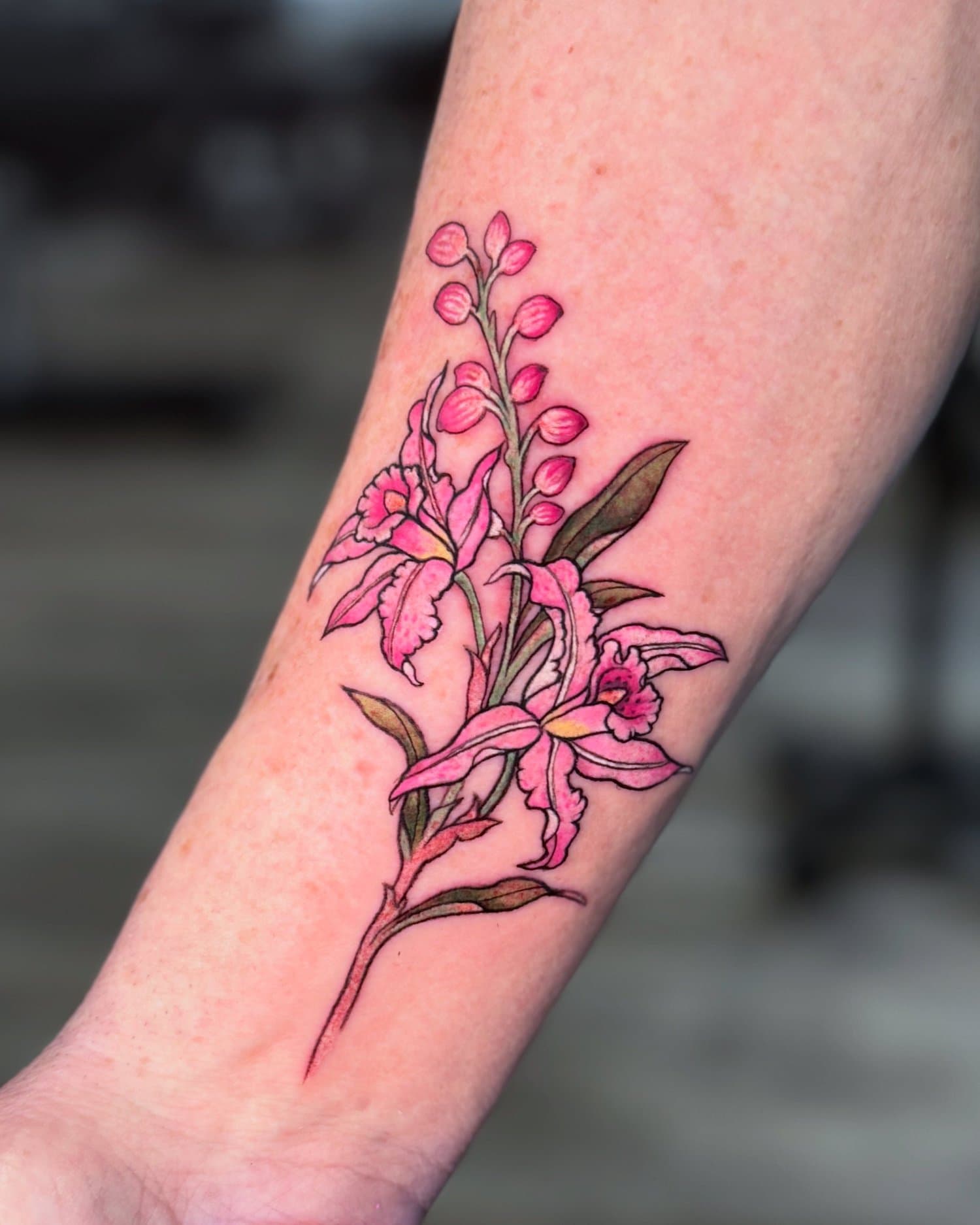 Colorful tattoo of pink lilies with green and brown leaves on a person's forearm.