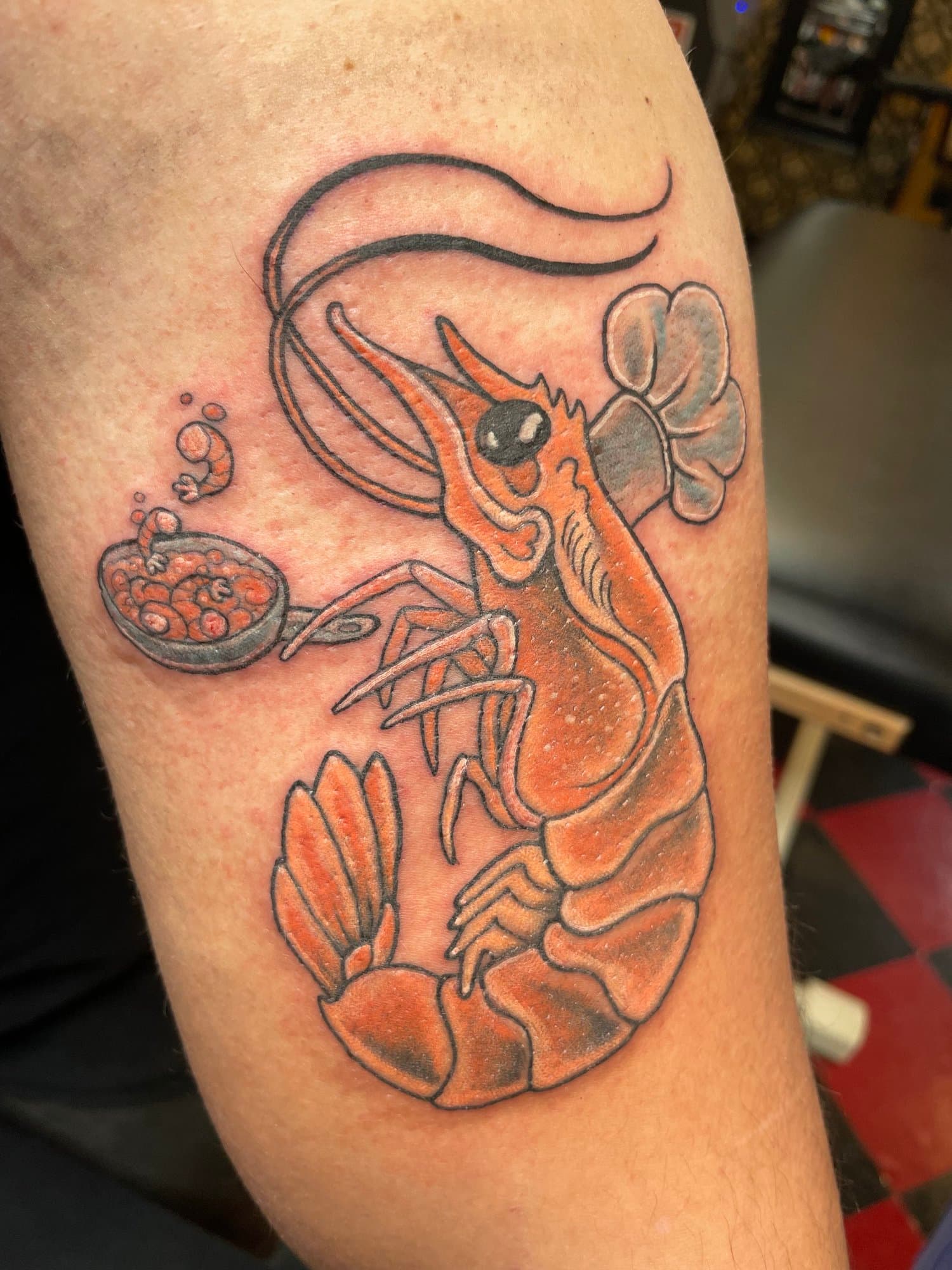 A colorful tattoo of a clownfish and a shrimp holding a bowl of food, with the shrimp wearing a chef's hat.
