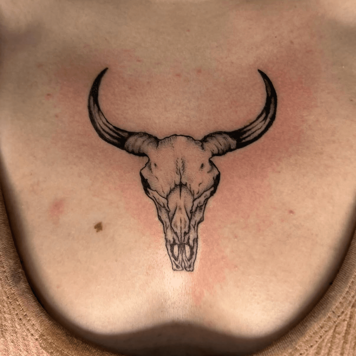 Fine black linework bull skull tattoo on a sternum, attributed to Luca on his Jade and Dagger profile page
