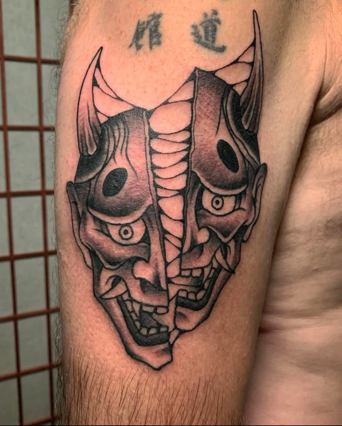 Black and grey hanya mask tattoo on upper arm.
