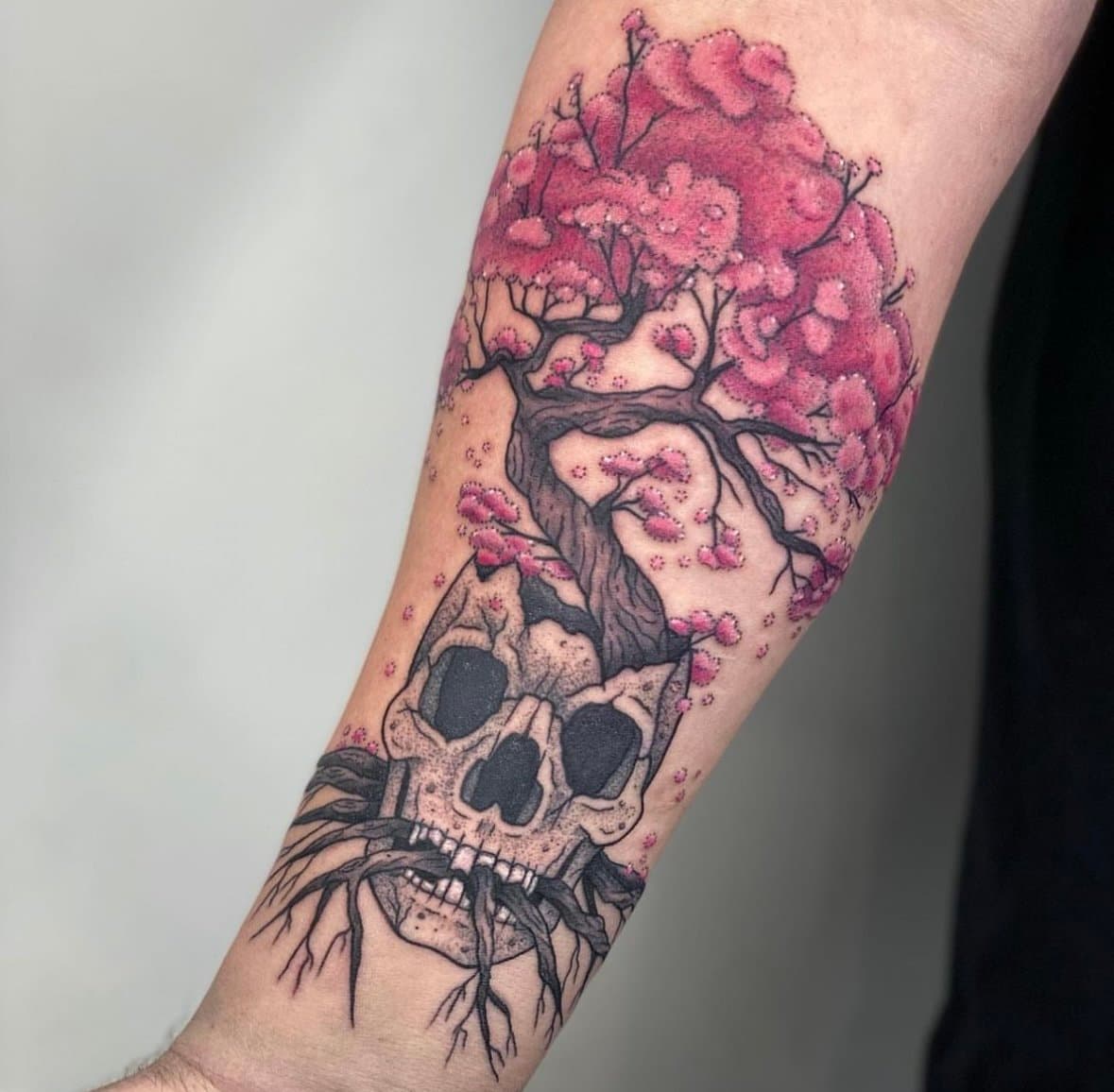 Forearm tattoo of a pink-blossomed tree growing from a black-and-grey skull