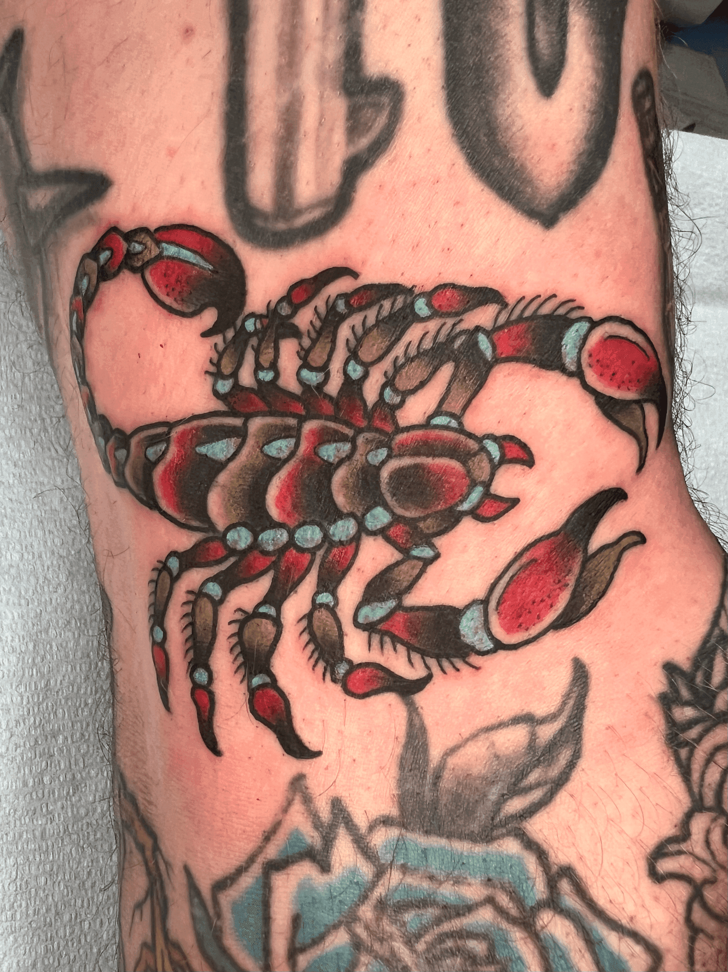 Tattoo of a colorful scorpion on a person's arm with additional tattoos visible around it.