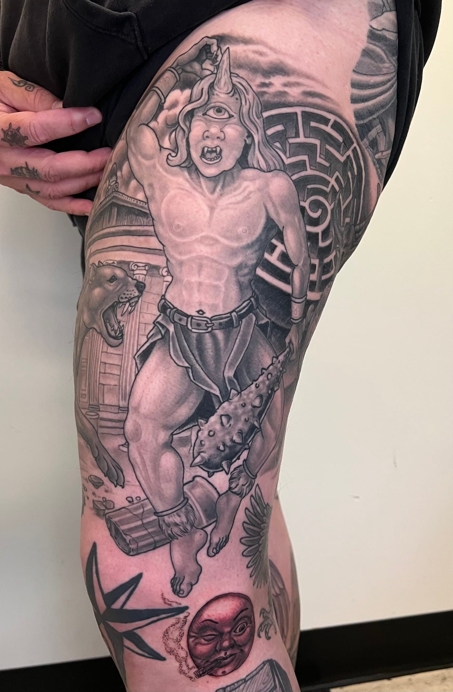 Black-and-grey warrior figure with a maze background tattooed on a hip and thigh