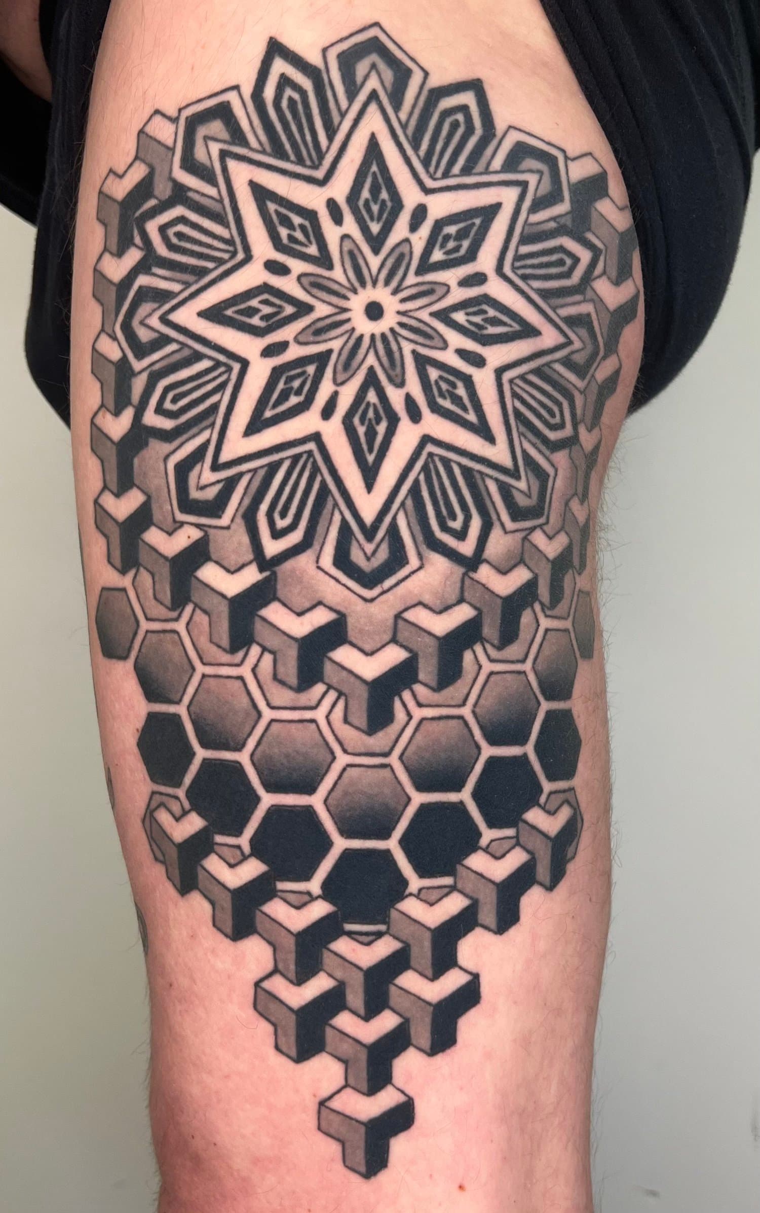 Black-and-grey geometric star and honeycomb pattern tattooed on an upper arm