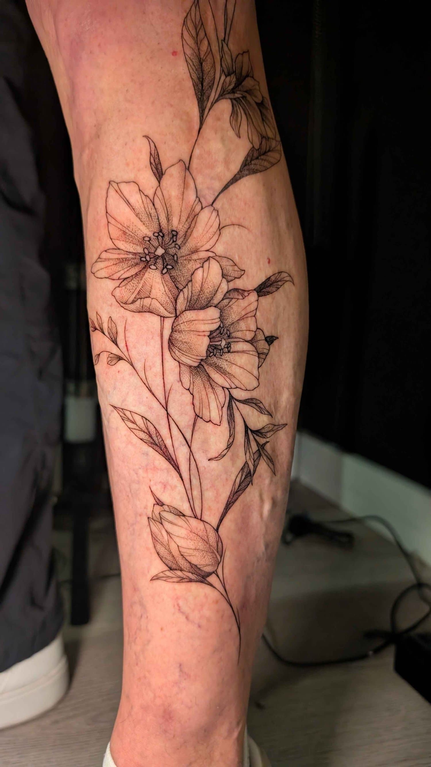 Fine black line and dotwork arrangement of poppies and leaves along the forearm