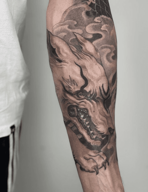 Detailed forearm tattoo of a snarling mythical creature with a wolf-like face and swirling background.