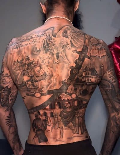 Large black and grey full back tattoo combining an eagle, mounted warriors and architectural scenes
